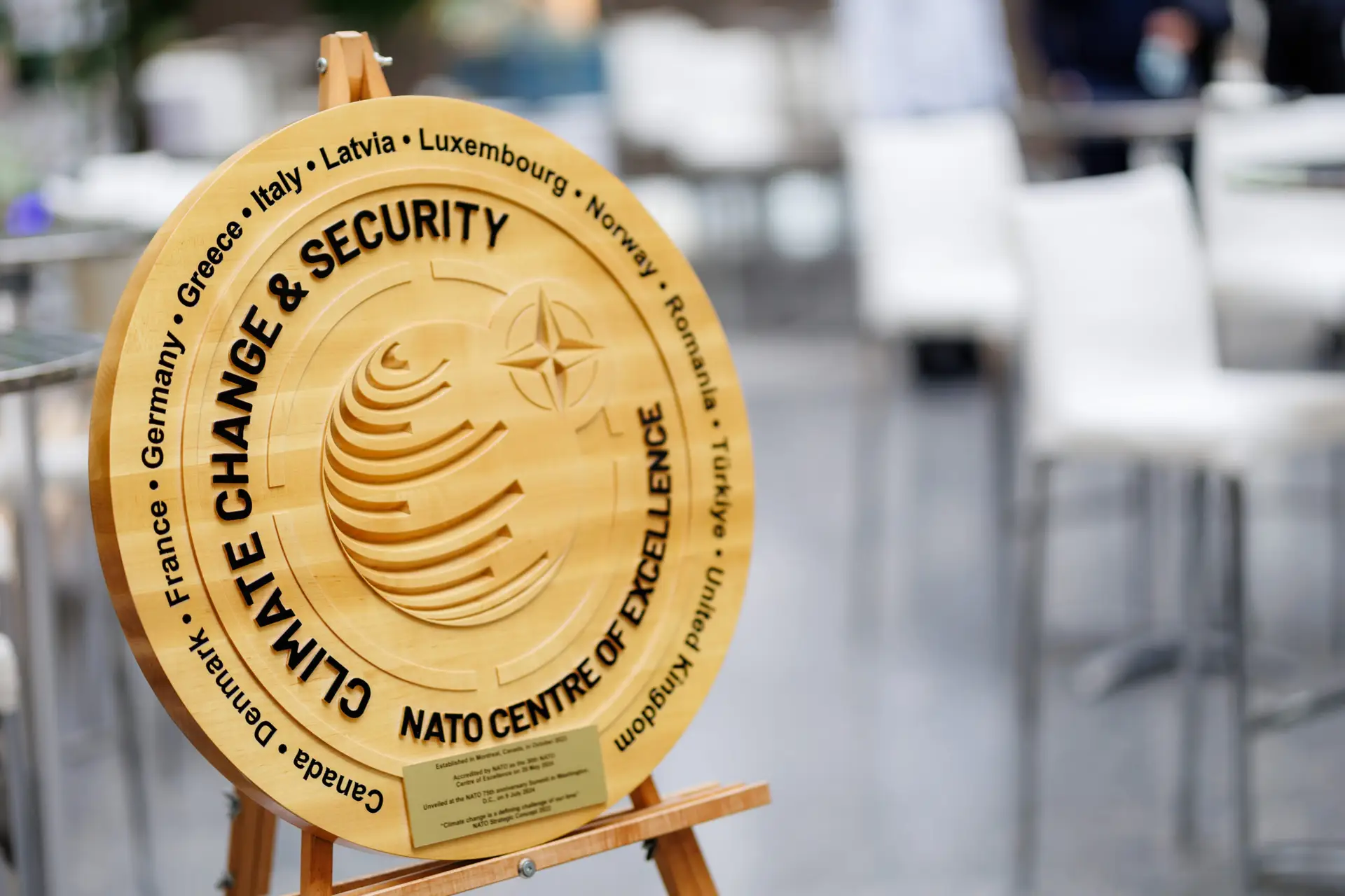 Wooden CCASCOE emblem on an easel featuring the text ‘Climate Change & Security – NATO Centre of Excellence,’